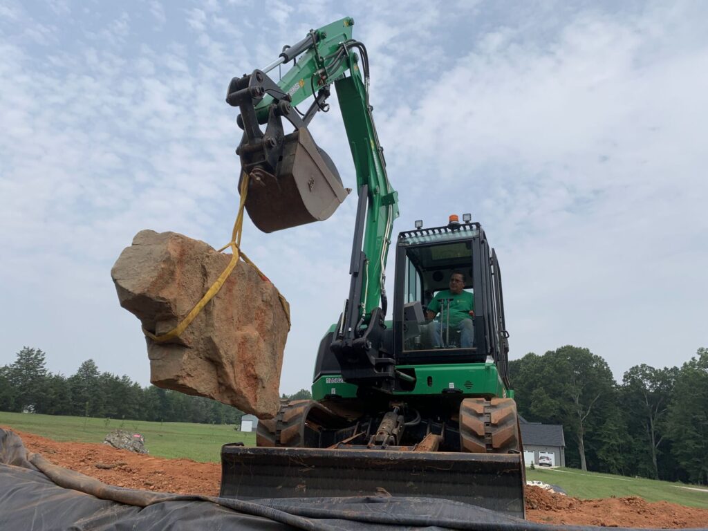 Moving a boulder into a recreational pond using an excavtor