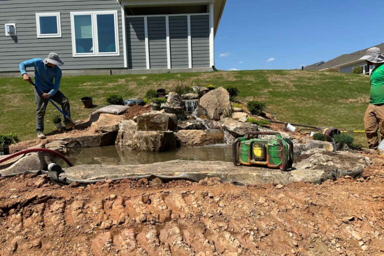 New backyard pond running for the first time with surrounding aquatic plants being added during final stages of installation in Encore at Streamside, Waxhaw, NC.