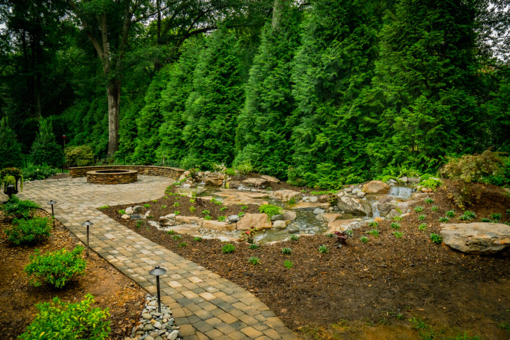 Full view of the pondless waterfall nestled into the backyard landscape, featuring cascading water over natural stone, framed by mulch beds and plantings for a serene and natural look.