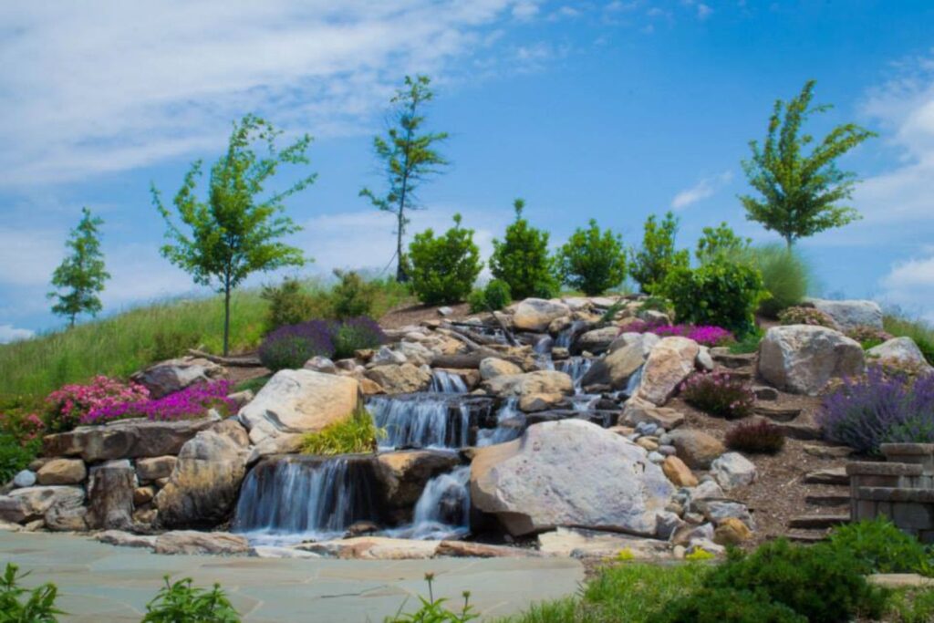 A large pondless waterfall built by Pondscapes of Charlotte, featuring dramatic water flow over natural boulders in a landscaped backyard setting.