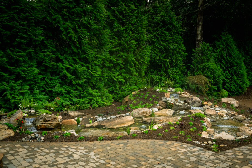 Completed pondless waterfall with flowing stream, surrounded by natural stone and landscaping