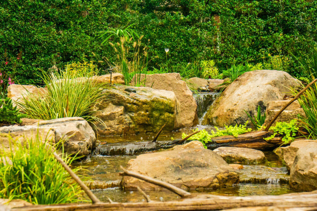 Custom pondless waterfall stream with natural cedar log detail in Marvin, NC backyard bird sanctuary