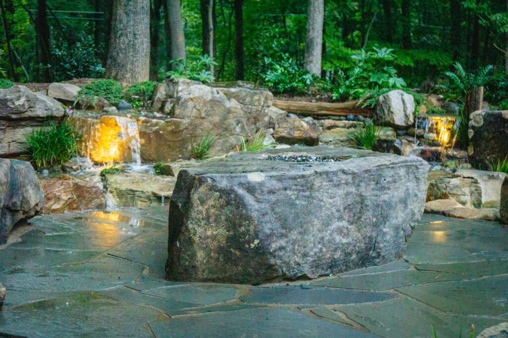 Fire boulder on flagstone patio surrounded by waterfall stream in Weddington NC backyard