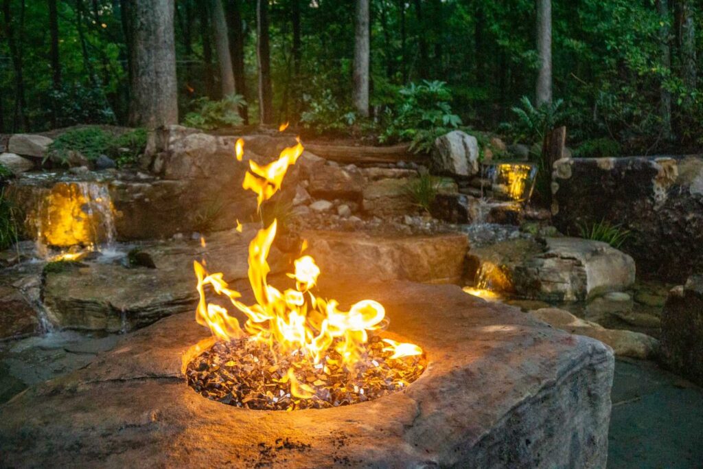 Professional waterfall and pond installation featuring fire boulder accent and custom stonework patio in Weddington, North Carolina by Pondscapes of Charlotte