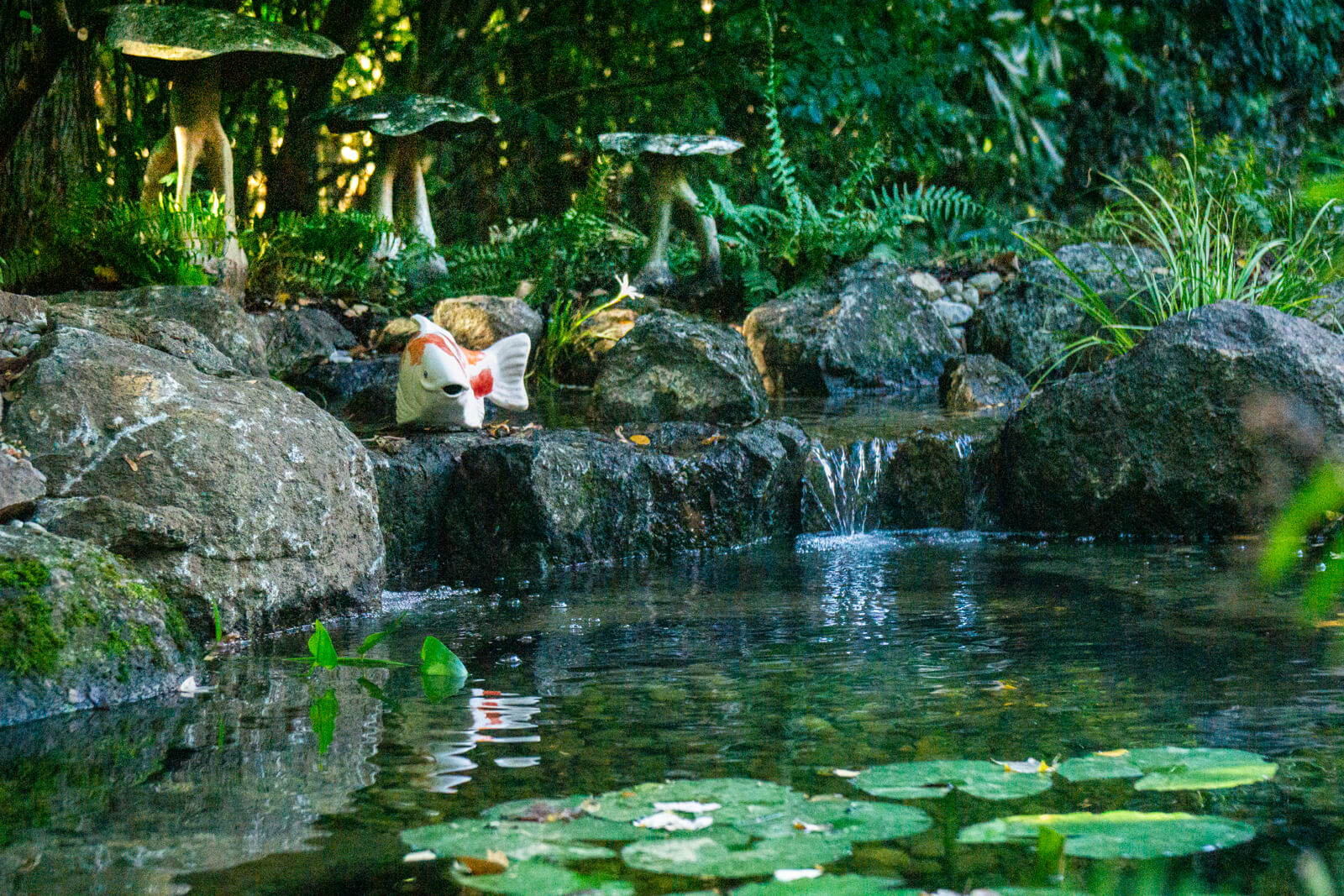 Natural stone waterfall flowing into backyard koi pond with decorative statue in Charlotte NC