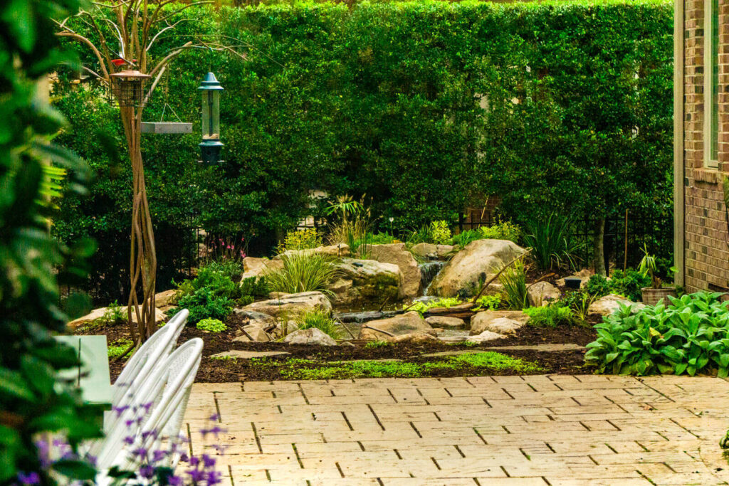 ondless waterfall with natural stone and aquatic plants next to patio in Marvin NC backyard