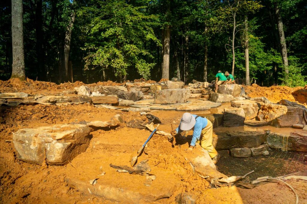 Natural waterfall and koi pond installation with fire boulder and stone patio in Weddington, NC backyard by Pondscapes of Charlotte