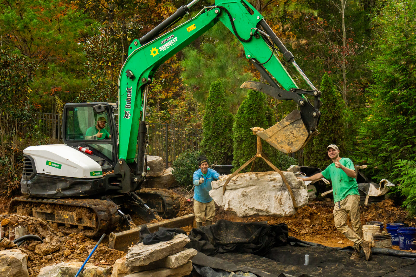 Pond builders constructing custom backyard waterfall installation with natural stone in South Carolina