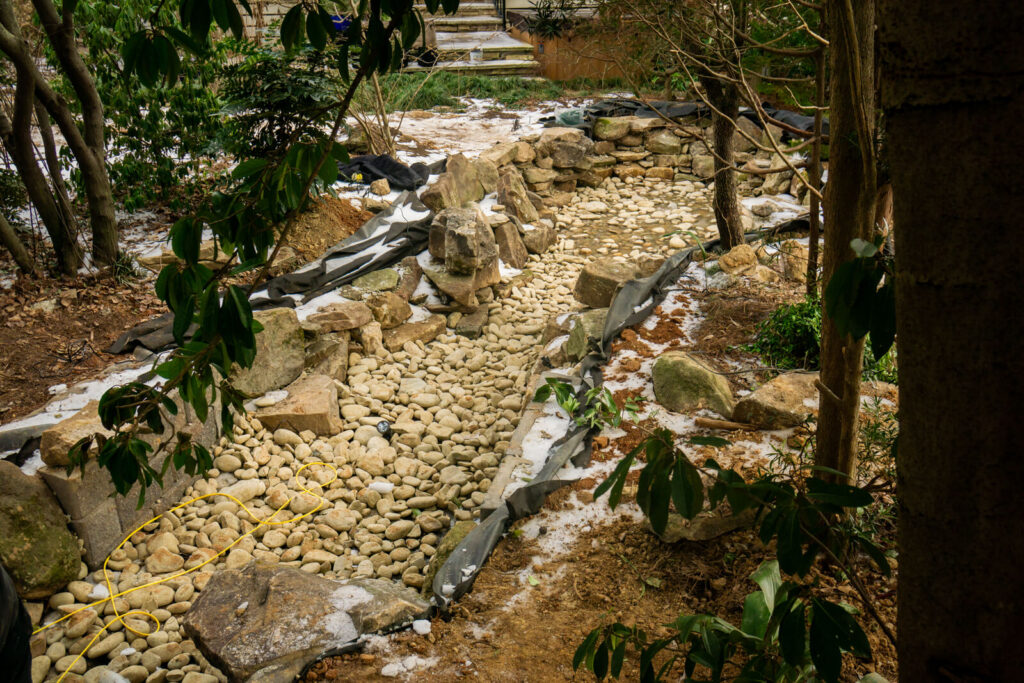 Stream style pond construction with liner and boulders in Matthews backyard
