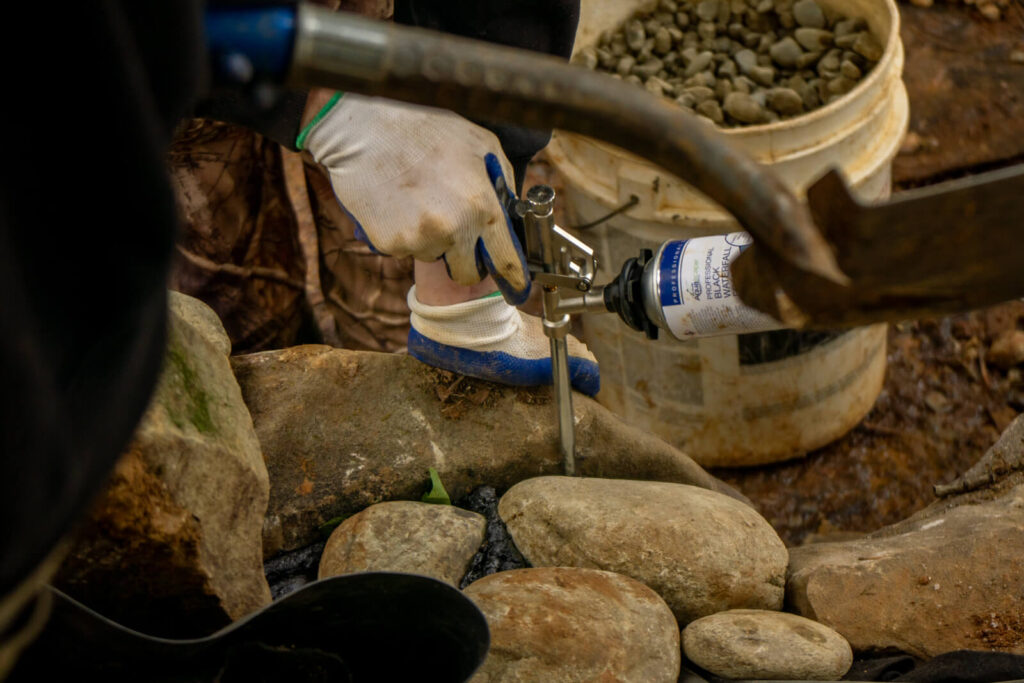Pond builder applying Aquascape waterfall foam sealant during construction in Matthews, NC