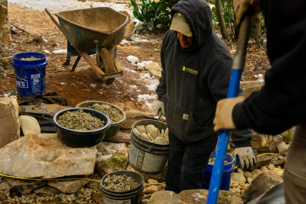 Pond builder moving stones while building stream style pond construction in Matthews