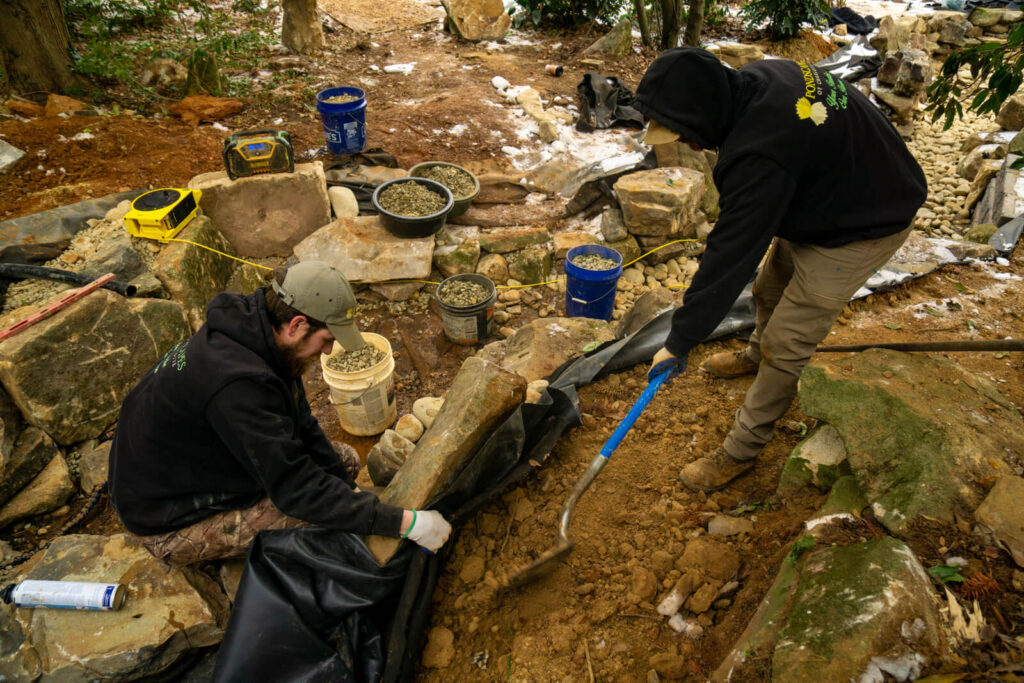 Pond builders backfilling and installing liner during backyard pond construction in Matthews, NC
