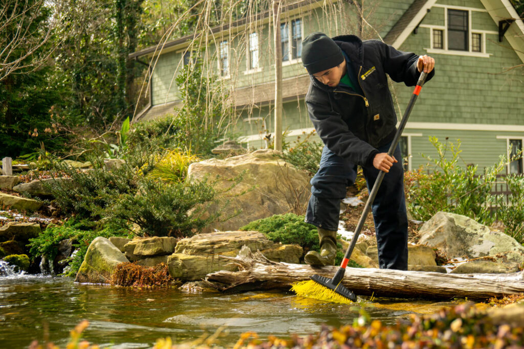 Pond technician brushing algae and debris off rocks to maintain waterfall