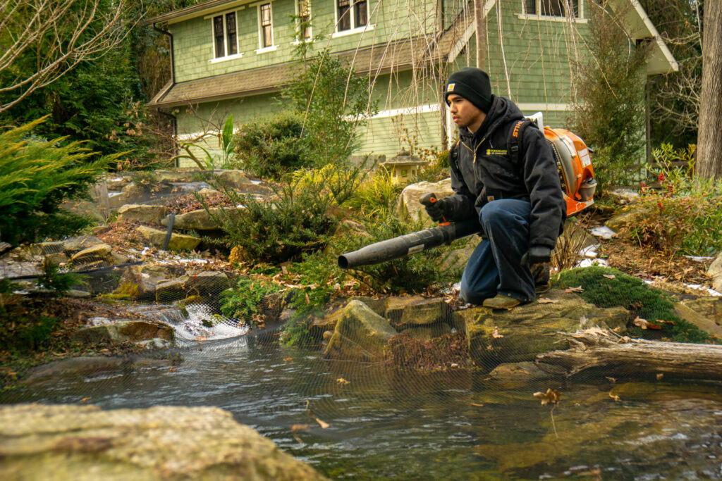 Pond technician blowing debris off waterfall during winter service visit