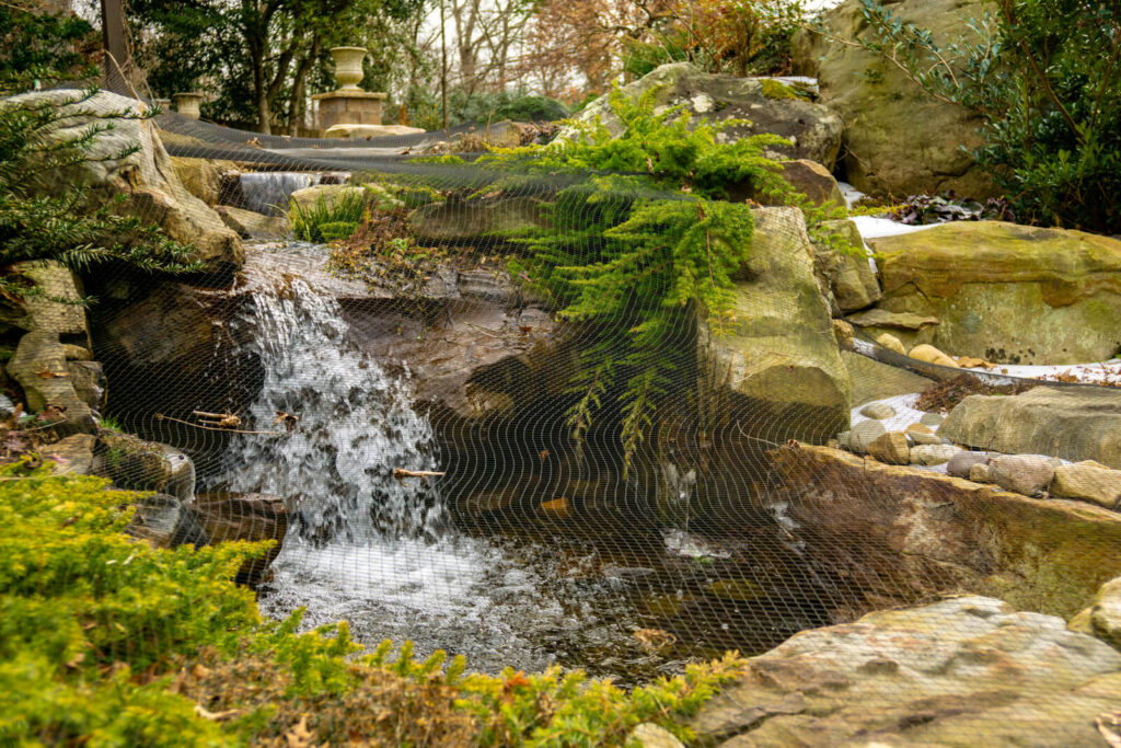 Natural stone waterfall with moss and netting during winter maintenance