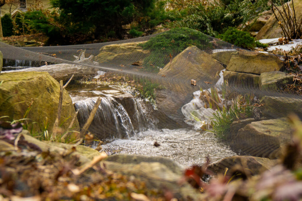 Close up of pond waterfall with protective netting during winter season