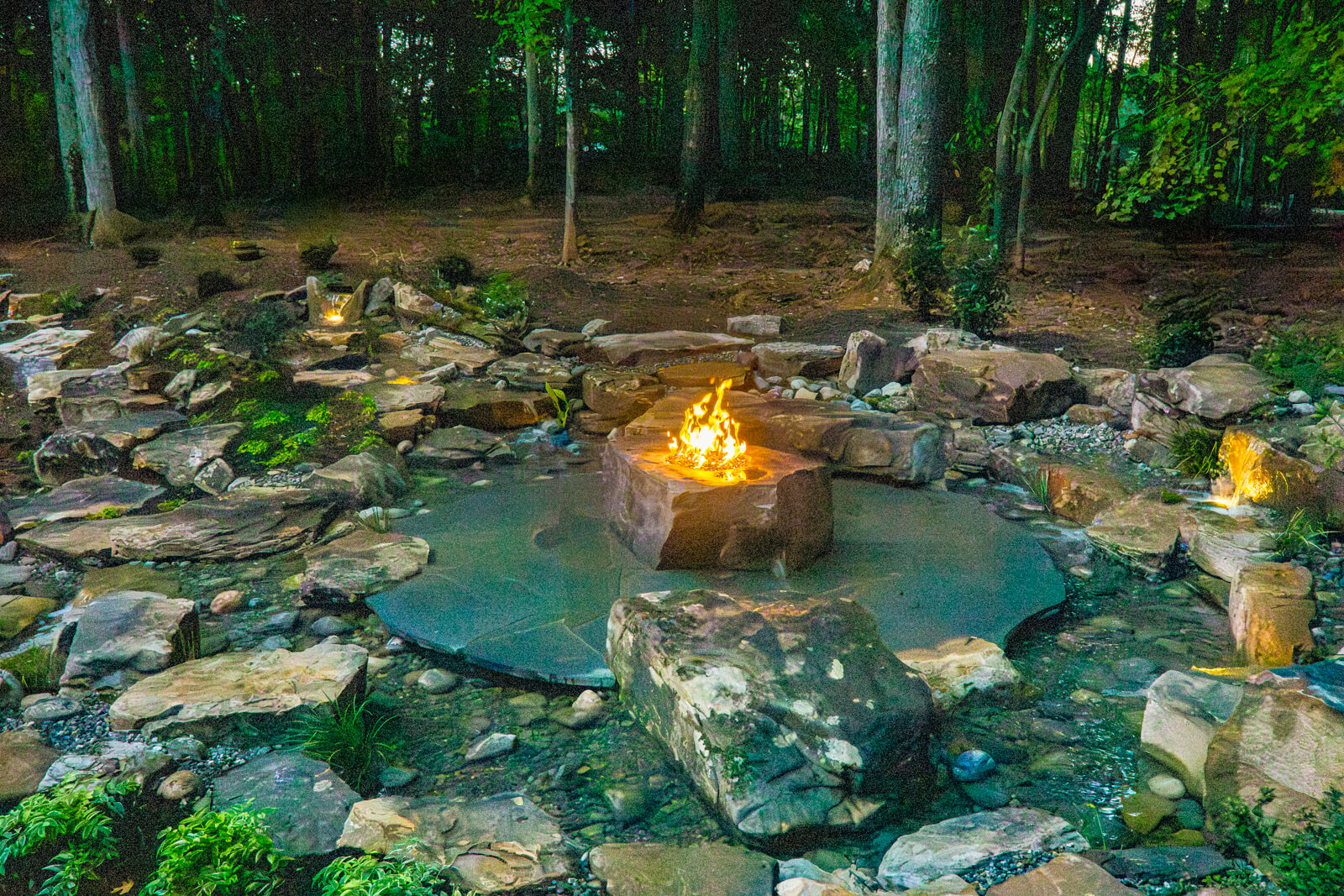 Award winning pondless waterfall with fire boulder and landscape lighting at night in Weddington NC