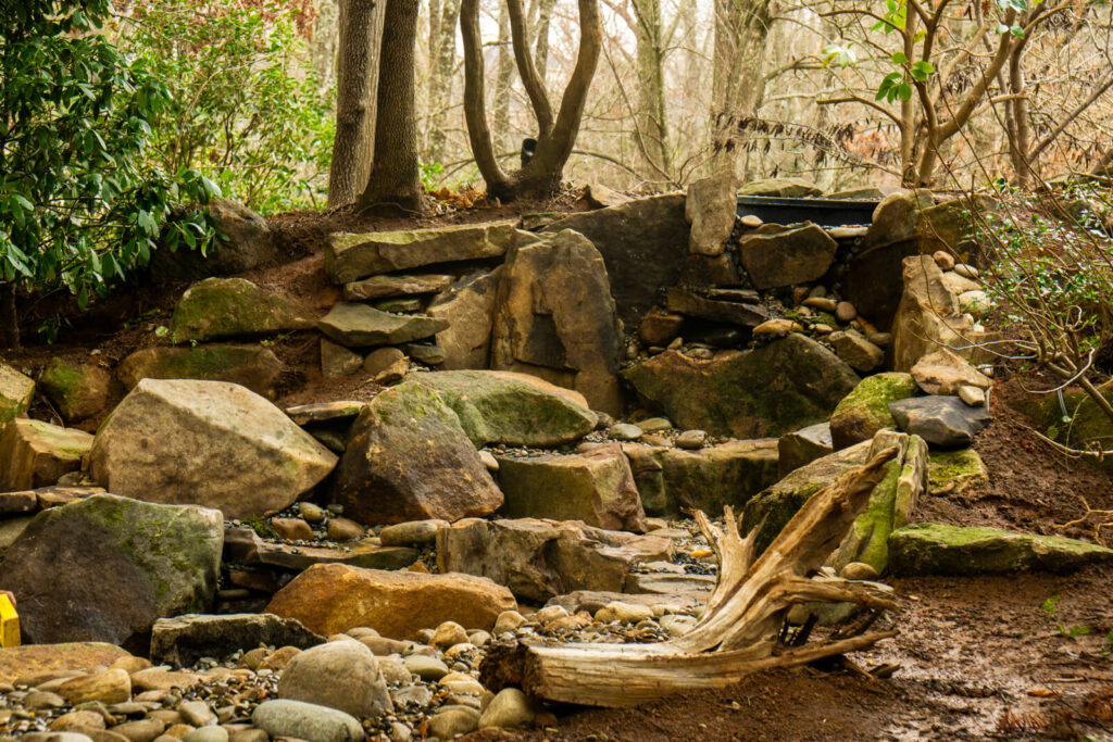 Natural stone waterfall structure with river rock stream bed during pond rebuild Matthews NC