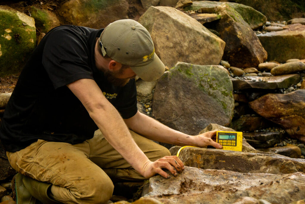 Professional pond builder checking pond depth with digital depth meter during stream pond build Matthews NC