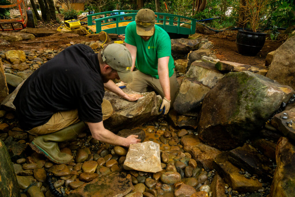 Water feature builders placing stepping stones in a stream style pond in Matthews, NC
