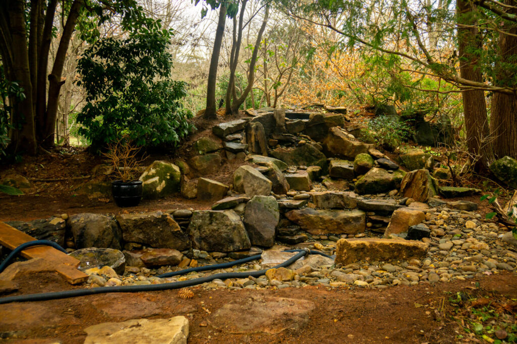 Large natural stone waterfall structure mid construction during backyard stream style pond build Matthews NC