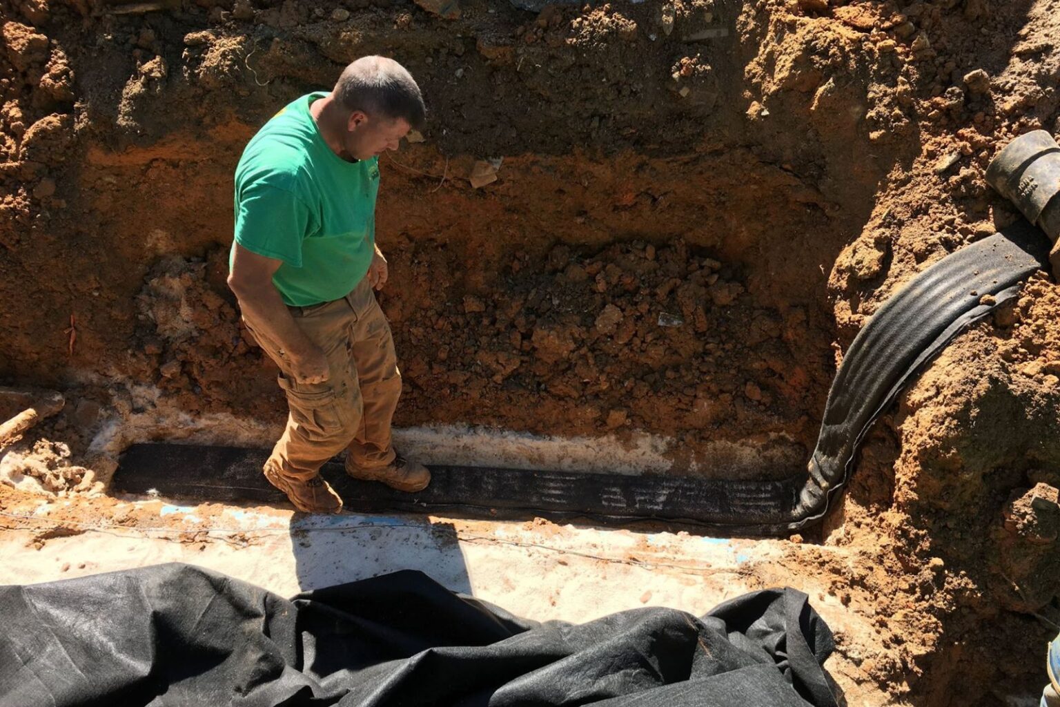Pondscapes of Charlotte technician installing flat drain under commercial pond to prevent water buildup Matthews NC