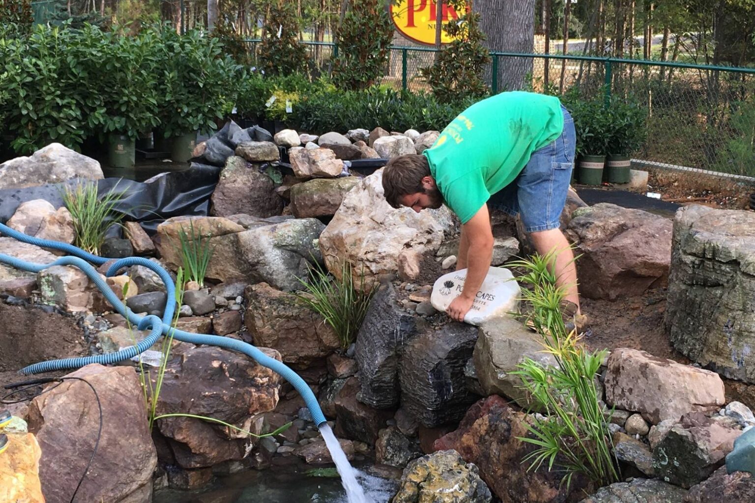 Pondscapes of Charlotte technician placing signature rock during commercial pond build at Pike Nurseries Matthews NC