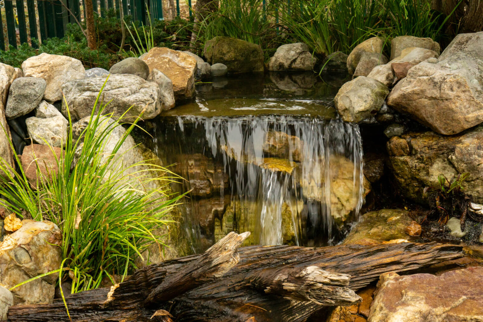 Natural waterfall flowing over large boulders into clear pond at Pike Nurseries Matthews NC