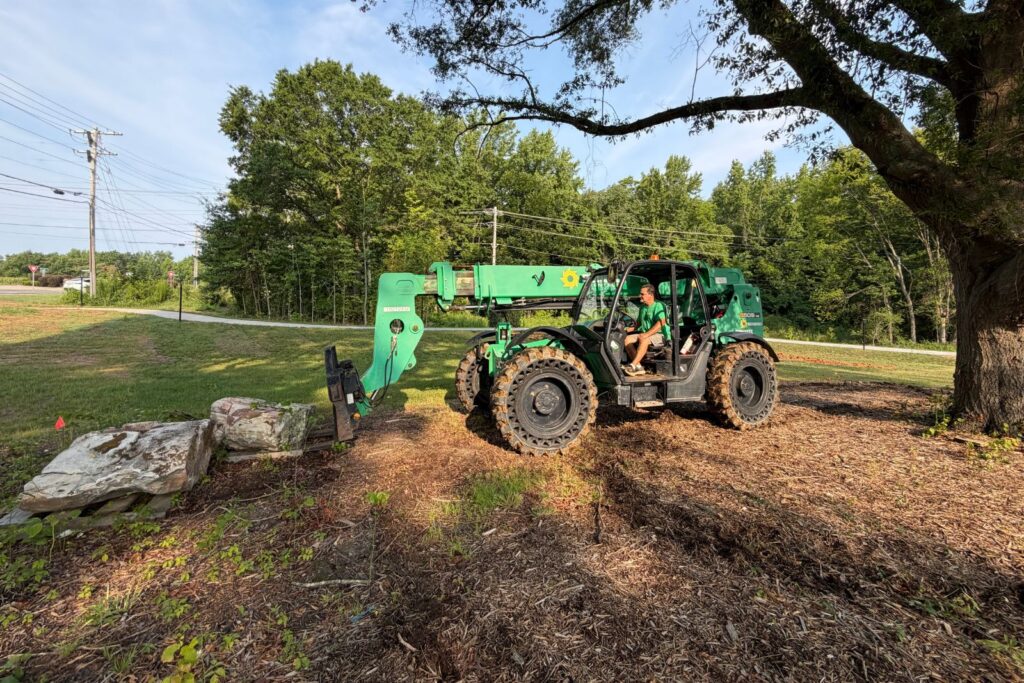 Crew member uses excavator to lift rocks on site.