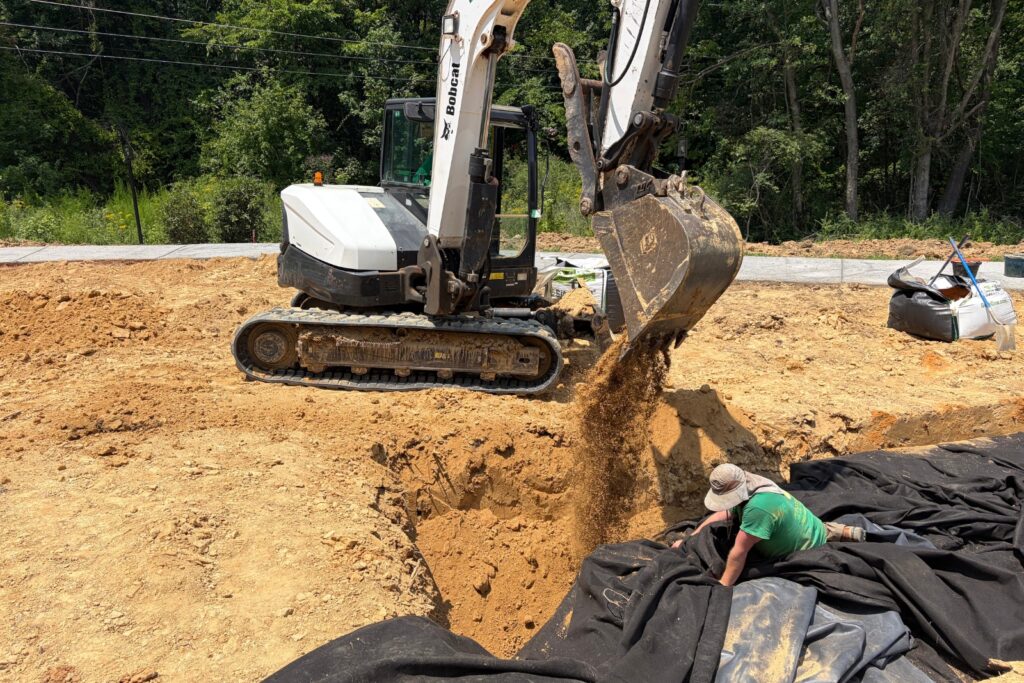 Crew member using excavator to adjust pond liner into place.