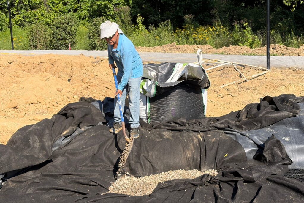 Crew preparing lined are with drainage gravel for new rainwater harvesting system.