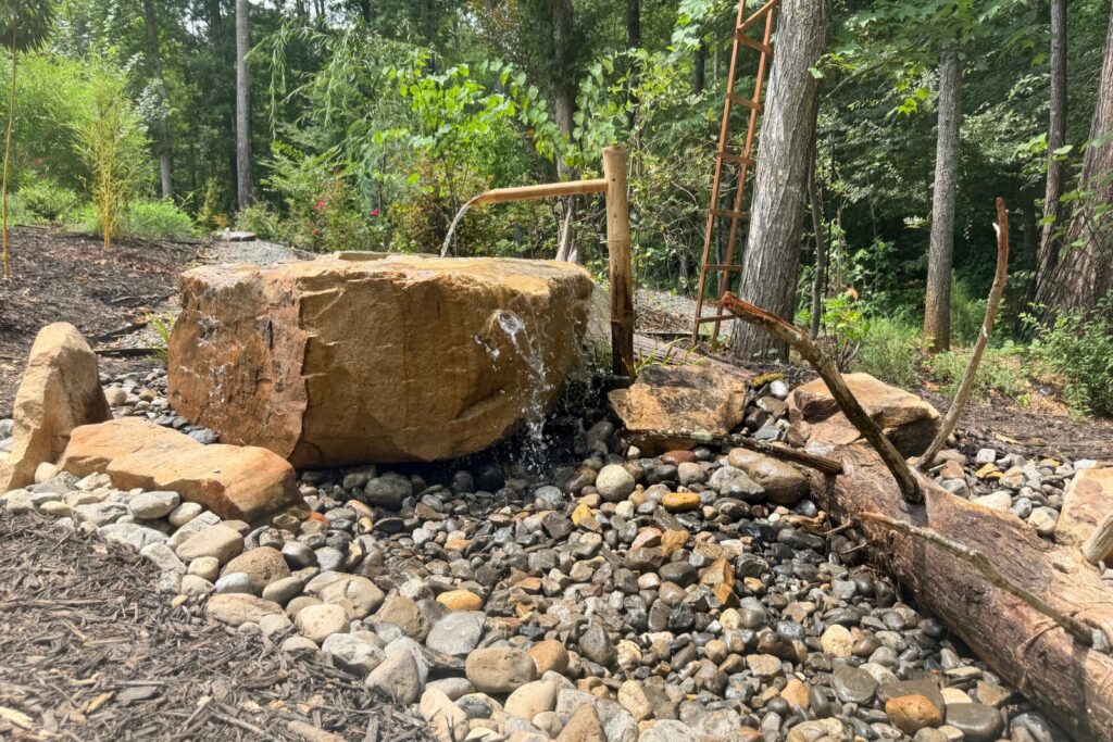 Bamboo spout pouring water on top of a large carved out boulder