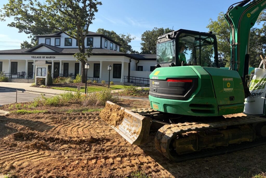 Excavator sits on a construction site in front of the Village of Marvin.