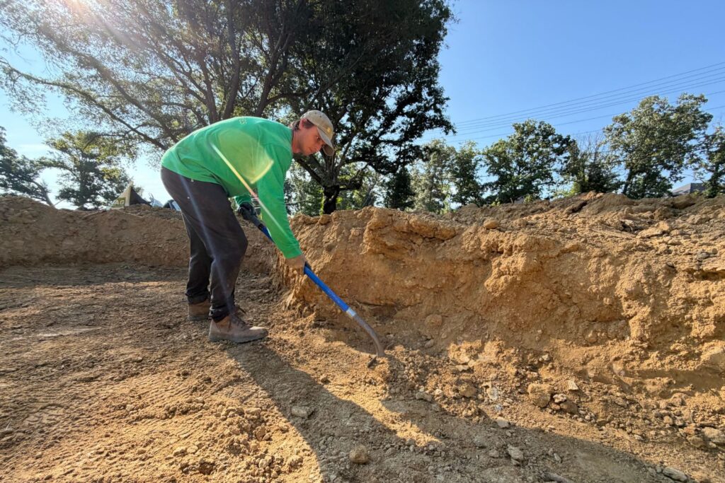 Crew member levels soil inside an excavation area at the construction site.