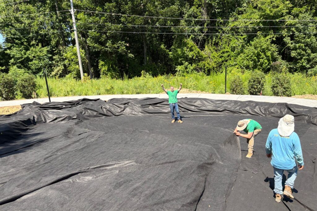 Crew members position and secure pond liner inside an excavated basin.