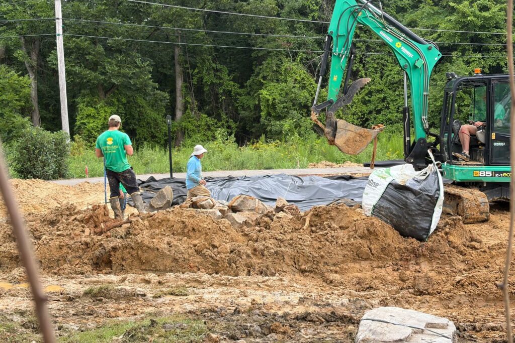 Excavator and crew members install large rocks for new water feature in Marvin, NC.
