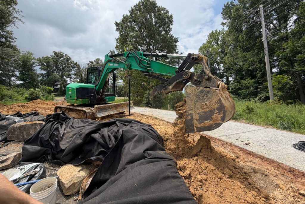 Excavator performs grading and soil shaping around a custom ecosystem excavator moving dirt and preparing the surrounding landscape for waterfall, stream, and pond construction.